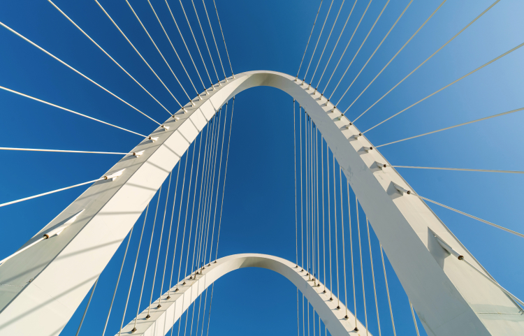 A white suspension bridge viewed from below, against a deep blue sky